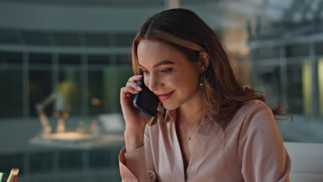 smiling businesswoman having phone conversation in glass night office closeup