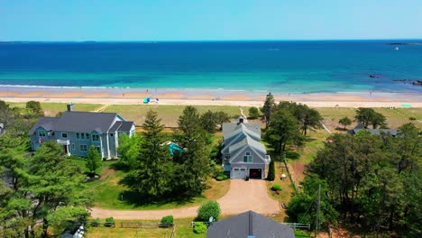 aerial drone view of a charming maine cottage. sandy yard, big windows, and an oceanfront deck create a beautiful beach house escape. prime real estate for summer fun and peaceful seaside living