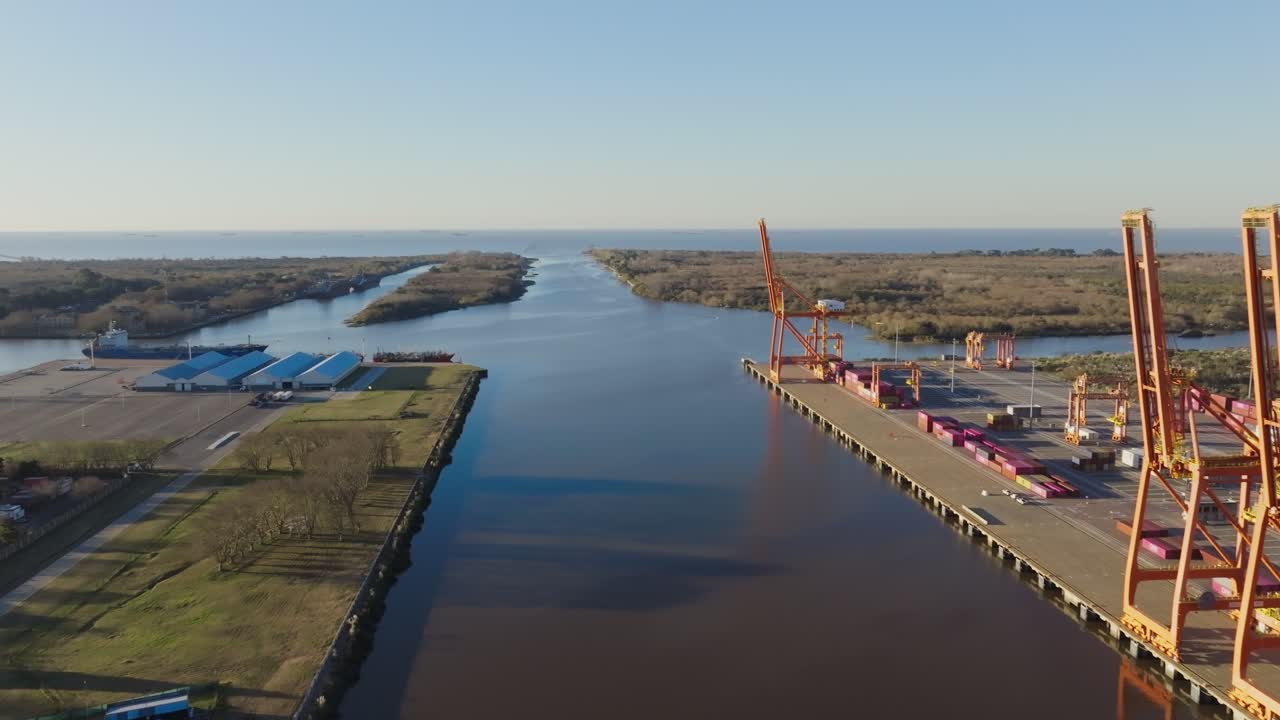 Drone captures a cargo ship at a river port during daytime, featuring cranes, docks, and active port facilities