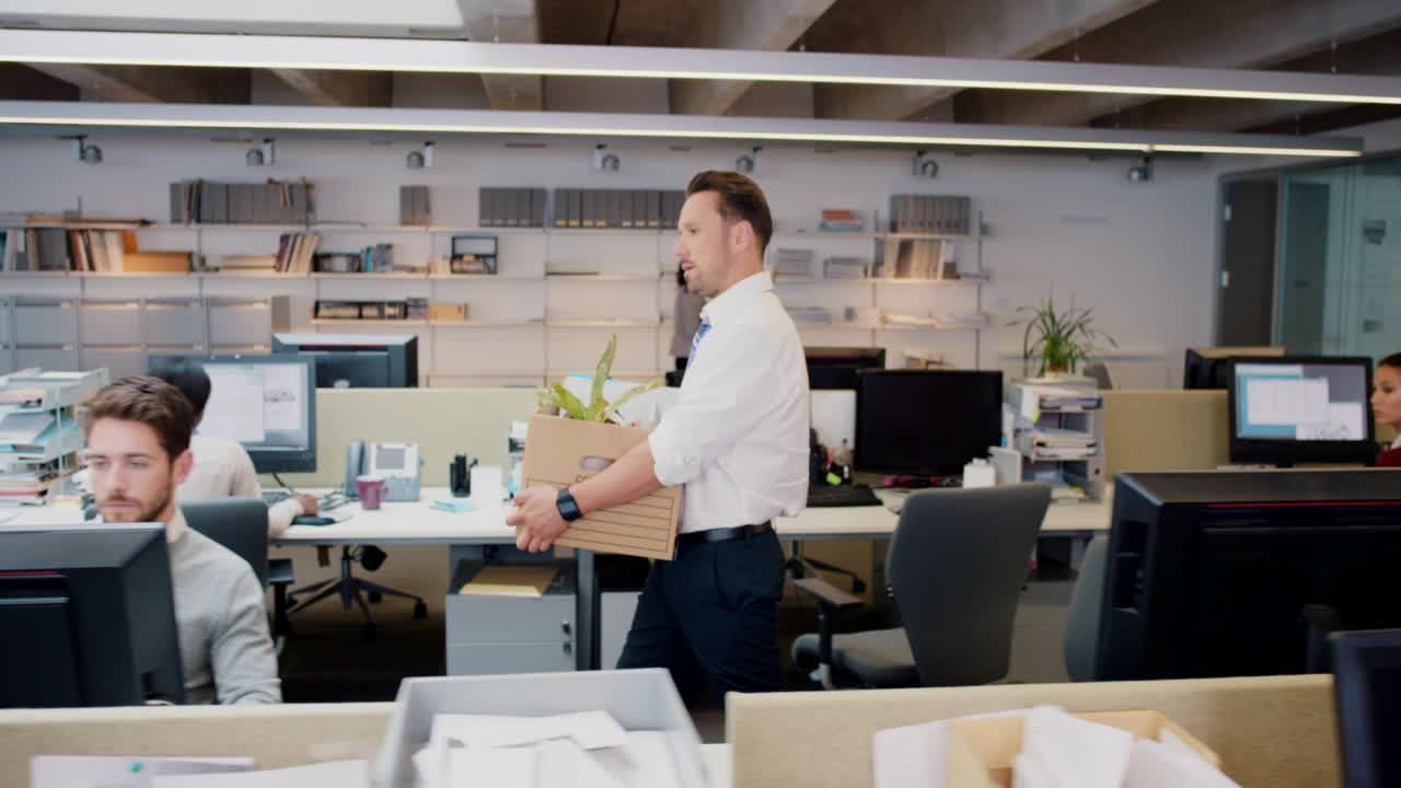 filmato in 4k di un bel giovane uomo d'affari che porta una scatola delle sue cose in ufficio dopo essere stato licenziato.
