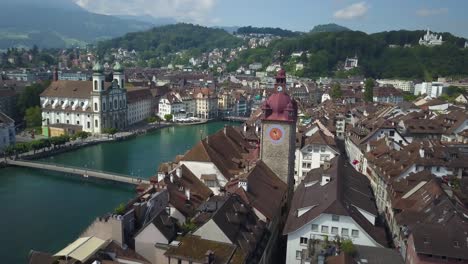 aerial orbit of lucerne old town picturesque rooftops, jesuit church, reuss river and bridges, surrounded by hills and forest at daytime, switzerland