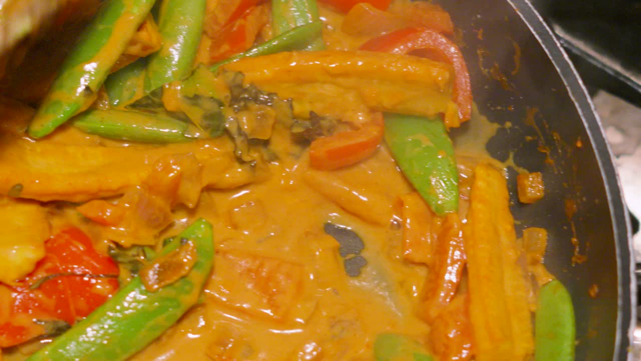 Healthy Spicy Red Thai Curry with Peppers, Sugar Snap Peas, Baby Corn is Stirred Around Hot Pan Cooking