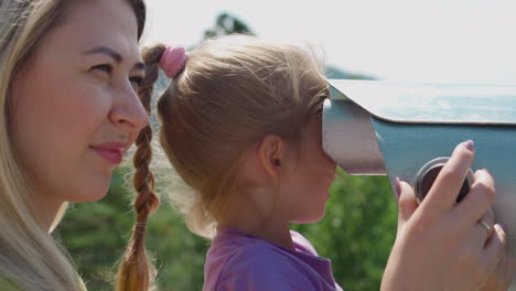 Girl-looks-through-binoculars-with-mother-on-view-point