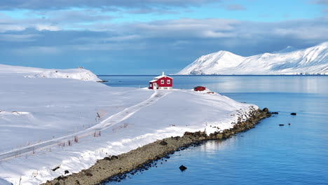 red house along fjord in iceland, in a snow covered landscape, aerial pan