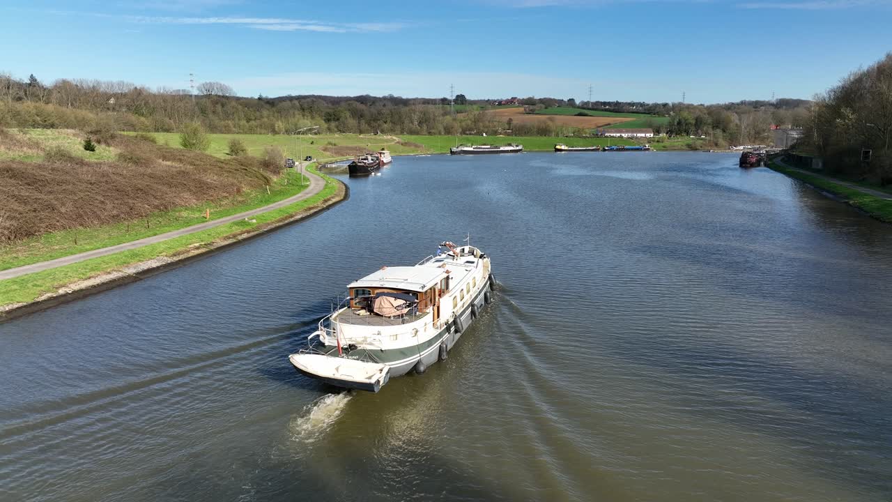 Aerial follow shot of a boat cruising along canal in Brussels, Belgium, surrounded by urban architecture under sunny skies