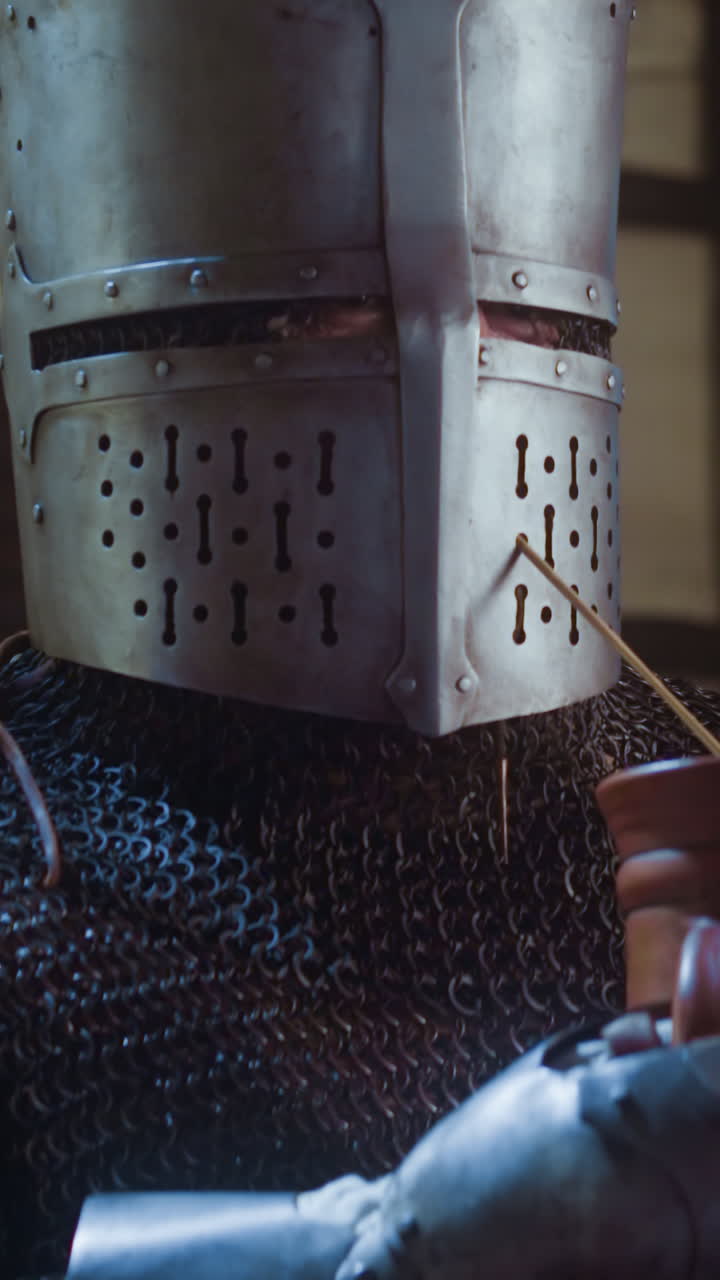 un caballero bebe cerveza a través de paja de planta en una taberna. un misterioso guerrero medieval evita el reconocimiento dejando el casco en la cabeza bebiendo en un pub.
