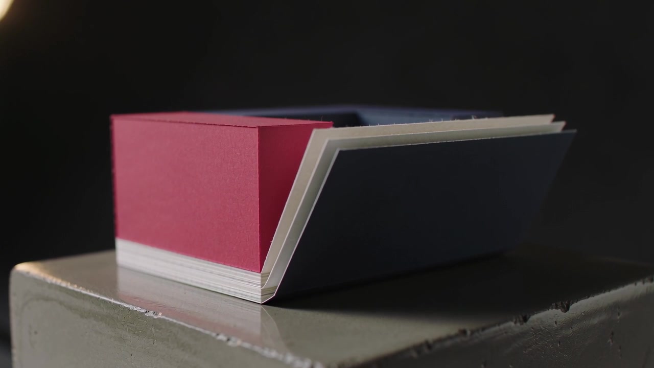 Sequence starting, lifting white sheets folding outward between red and blue paper blocks on plinth