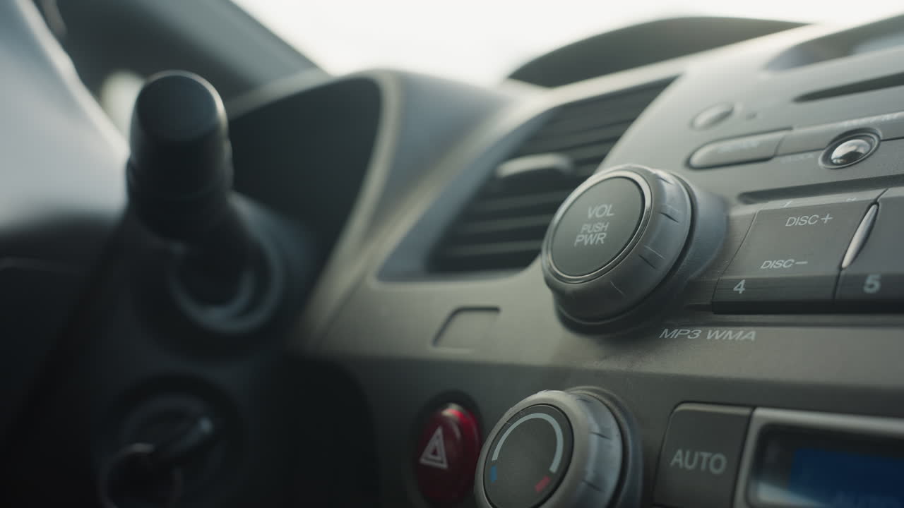 close up driver hand pressing car audio system play button to start mp3 playback on dashboard cd changer unit panel showing finger movement focus on metallic button knob interaction inside vehicle