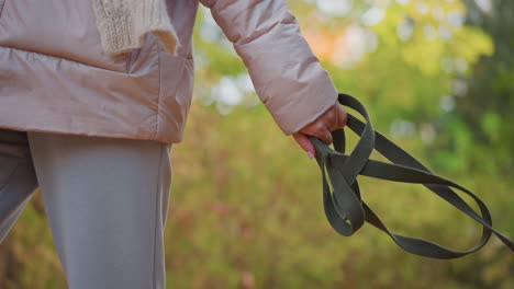torso shot of woman walking dog on autumn forest path, cozy jacket and scarf visible as she holds leash, crunchy leaves underfoot and soft sunlight filtering through foliage