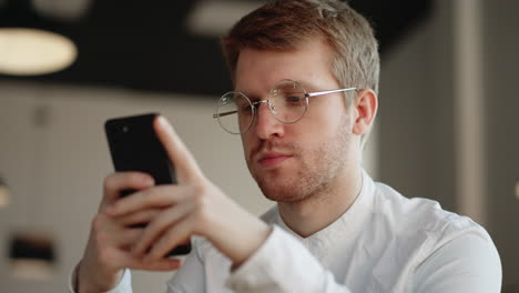 Un-Hombre-Atractivo-Con-Gafas-De-Pie-Solo-En-El-Interior-Sosteniendo-En-Las-Manos-El-Número-De-Marcación-Del-Teléfono-Inteligente-En-La-Pantalla-Táctil.-Mujer-Joven-Y-Alegre-Navegando-Por-Internet,-Navegando-Por-Internet,-Elige-El-Concepto-De-Compra-De-Productos-En-Línea