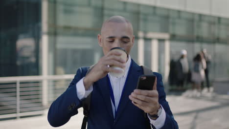 portrait-of-bald-hispanic-businessman-standing-looking-at-watch-using-smartphone-drinking-coffee-corporate-office