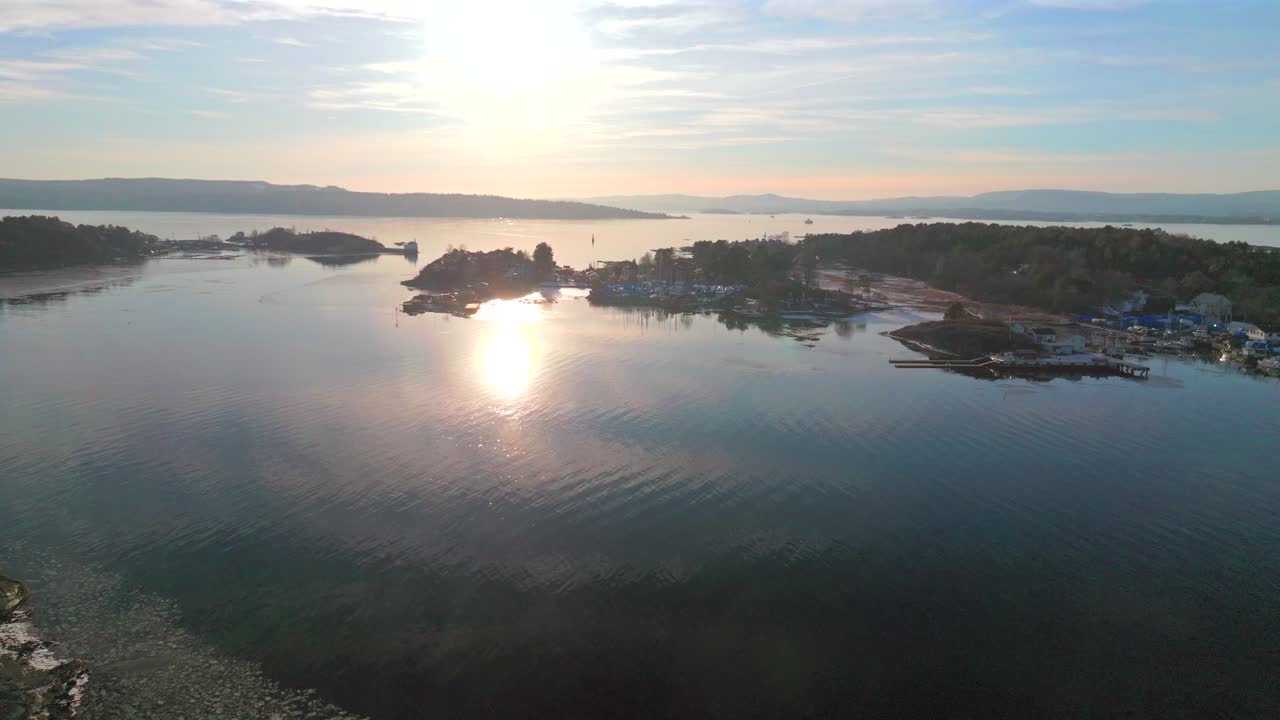 Sunset on horizon Hovedøya island Hovedoya Aker Brygge Lindøya aerial drone Norway Norge harbor ferry boat Norwegian Oslo Fjord frozen ice icy coastline sea calm peaceful salt water forward motion
