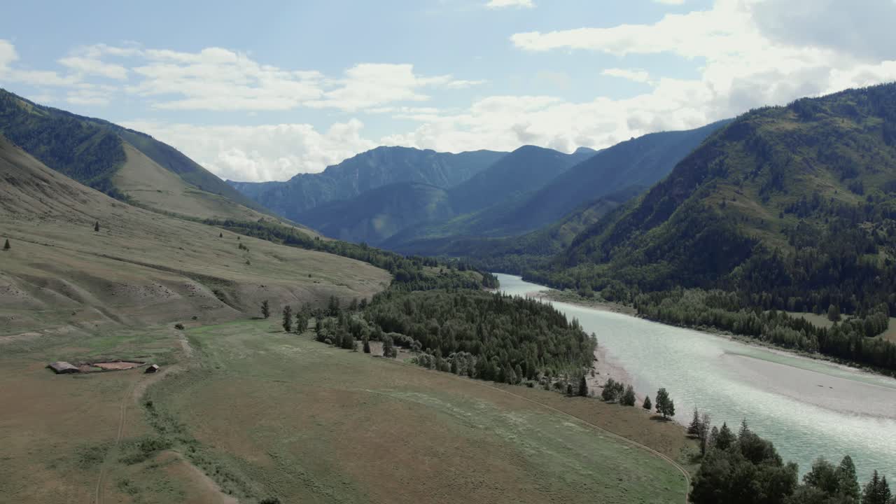 Drone footage of a wide river winding through Ak-Kem valley with forest and mountain slopes under a cloudy sky in Altai Republic, Russia, scenic wilderness landscape
