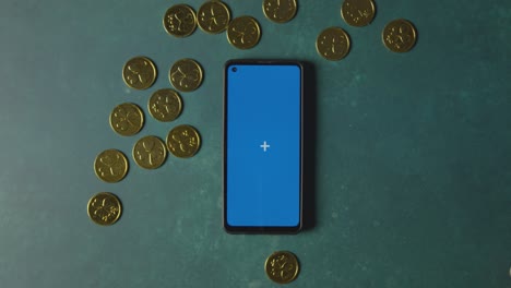 overhead studio shot of hand collecting gold coins and blue screen mobile phone to celebrate st patricks day