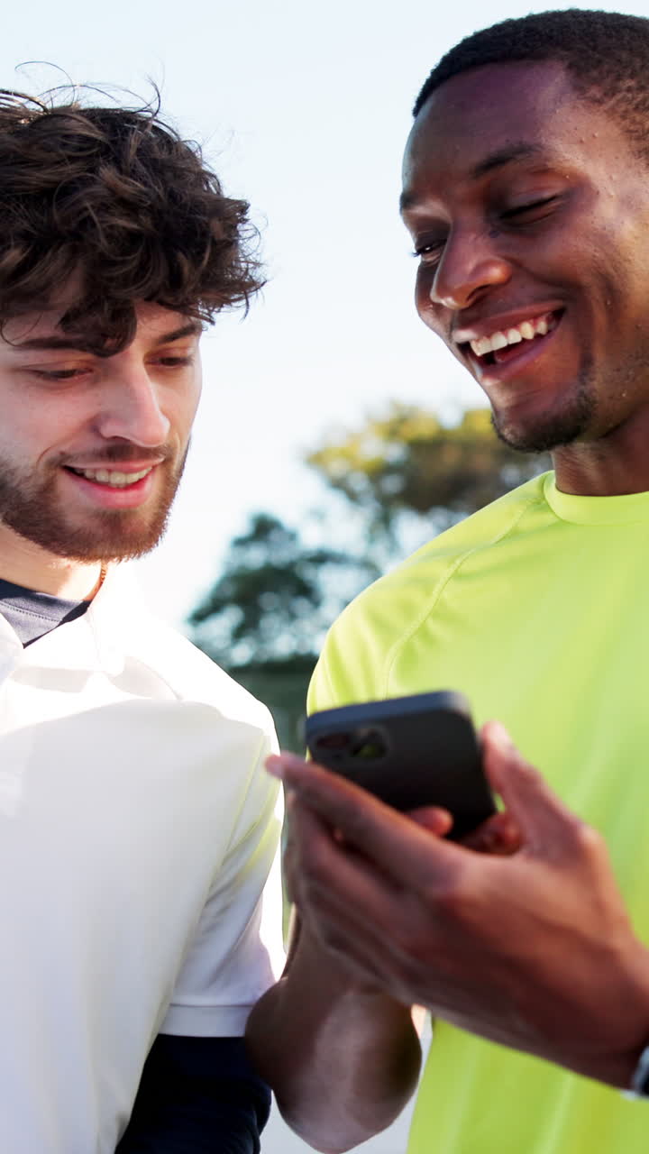 Dois jovens felizes sorrindo e olhando para um smartphone ao ar livre.