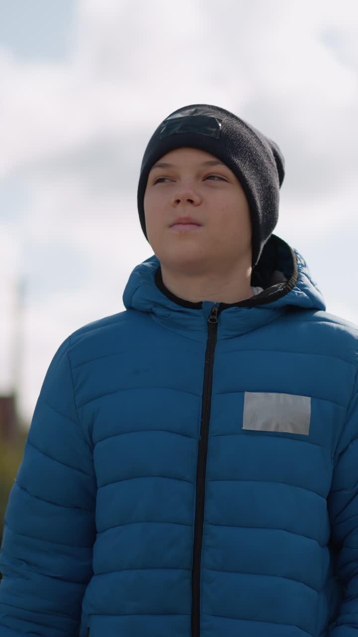 Close-up of white boy in blue jacket and black beanie strolling in residential area with a frowning face, reflecting subtle emotions against a backdrop of autumn colors