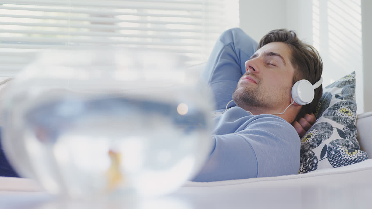 금색 물고기 그 ⁇ 과 소파에 누워 있는 남자가 헤드폰을 착용하여 음악 4k 4k를 나열하고 있습니다.