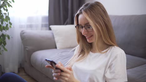 Beautiful-woman-chatting-on-her-phone-and-smiling,-sitting-on-the-living-room-s-floor-during-quarantine-time