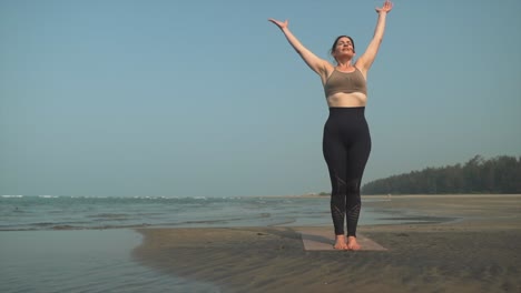 mujer de pie haciendo yoga estirándose en la orilla de una playa