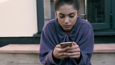 young asian teenager sitting on steps using her mobile phone