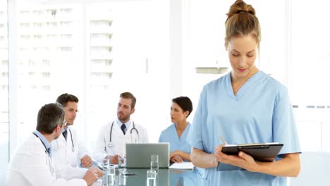 Nurse-smiling-at-camera-while-staff-are-talking-behind-her