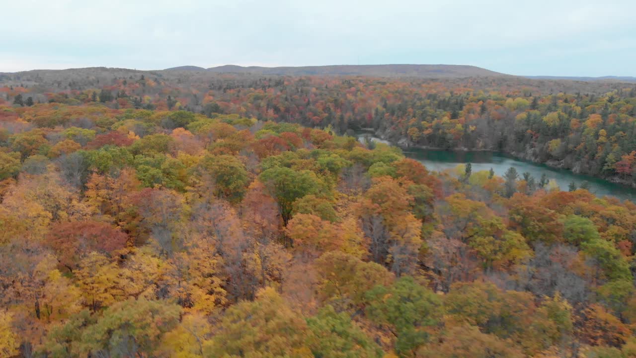 vuelo lateral sobre el lago rosa en gatineau hills quebec con montañas en el fondo y el lago en el medio y una carretera en primer plano en el otoño