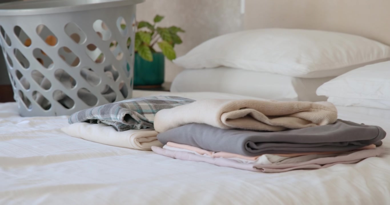 African man wearing headset seeing grey laundry basket folding laundry on bed to organize clothes