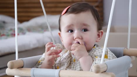 adorable baby girl playing with her pacifier while sitting on a baby swing - close up