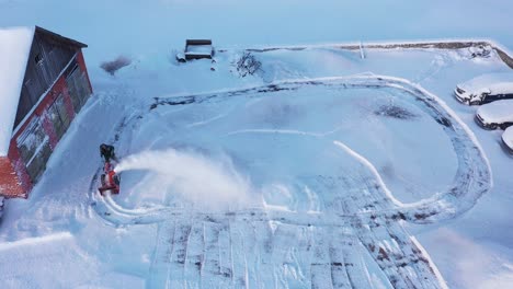 man plowing parking lot near farm building on cold winter day, aerial view