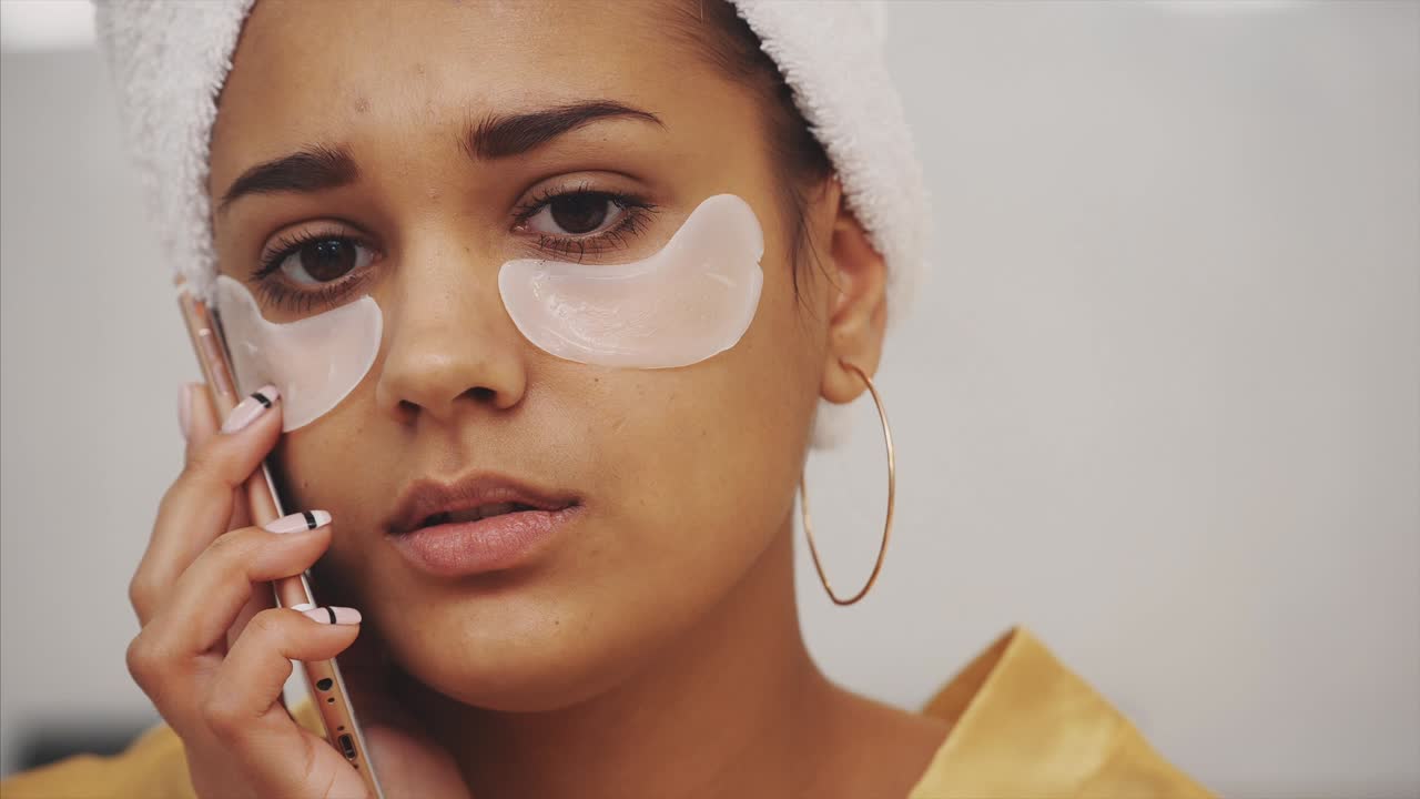 Closeup portrait of beautiful woman after bath with towel on head puts patches under the eyes from wrinkles and dark circles.