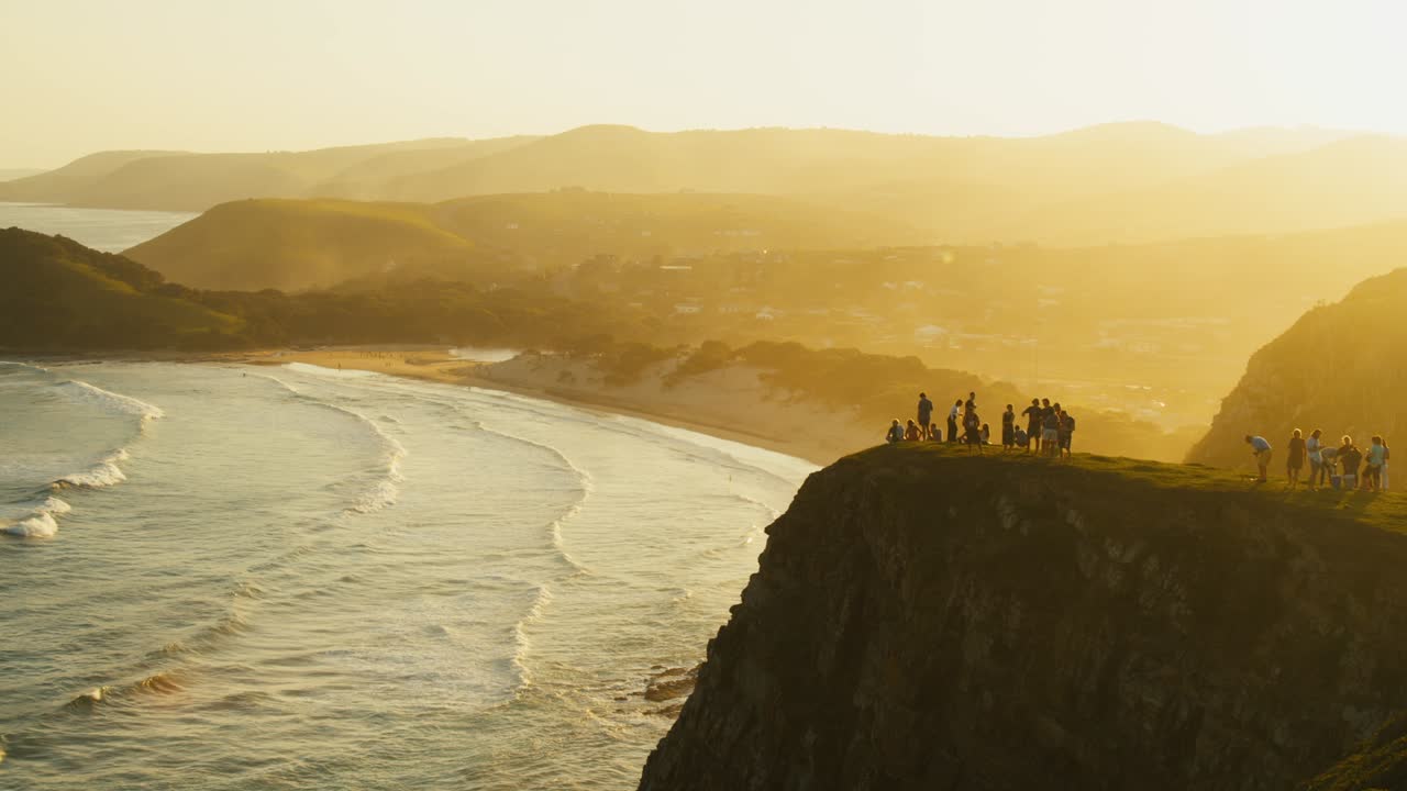 Group of people standing on a cliff with African sunset view
