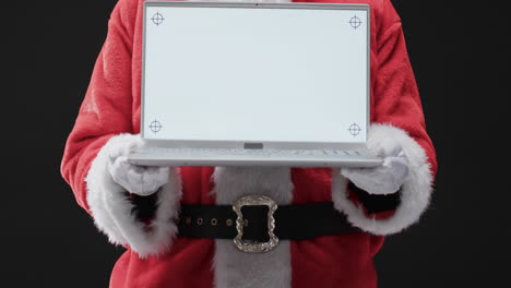 Video-Vom-Weihnachtsmann,-Der-Einen-Laptop-Mit-Kopierplatz-Auf-Schwarzem-Hintergrund-Hält