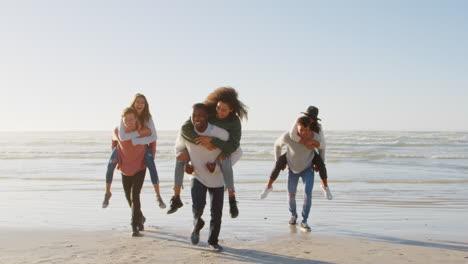 Gruppe-Von-Freunden,-Die-Gemeinsam-Huckepackrennen-Am-Winterstrand-Veranstalten