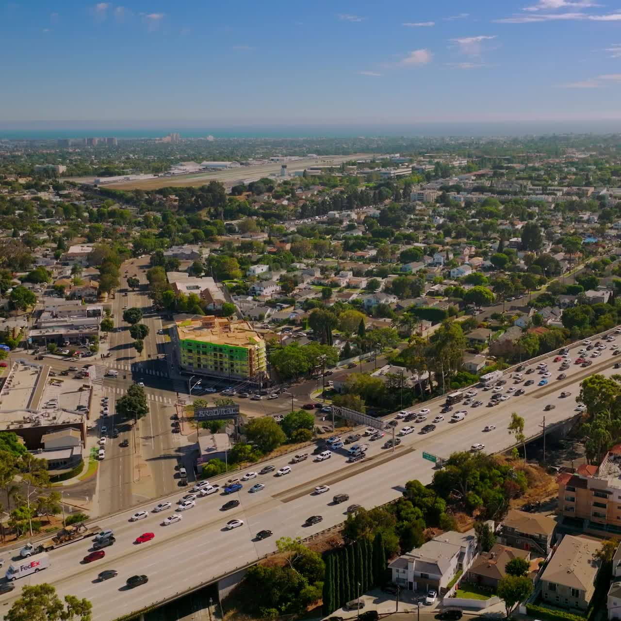 Beautiful sunny panorama of green district in Los Angeles. Drone footage over the motorway with busy traffic. Aerial view