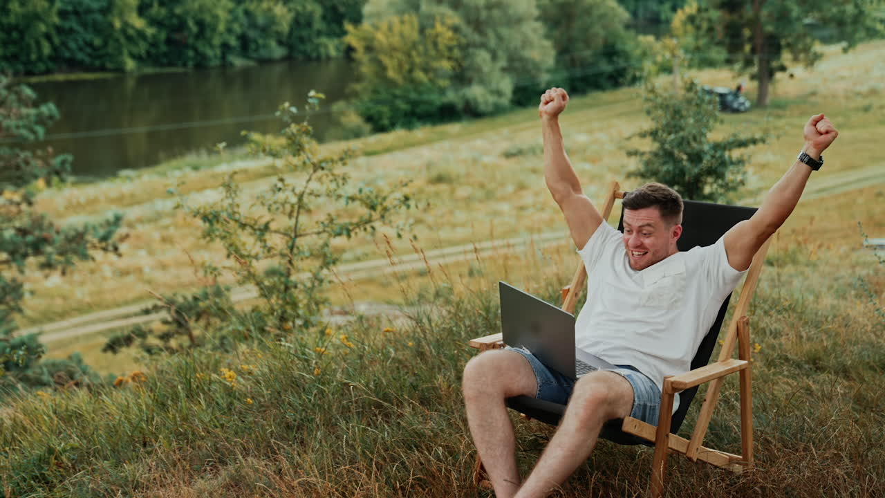 Succeeding at work. Happy Caucasian man rejoices looking at the screen of laptop. Freelancer working in nature.