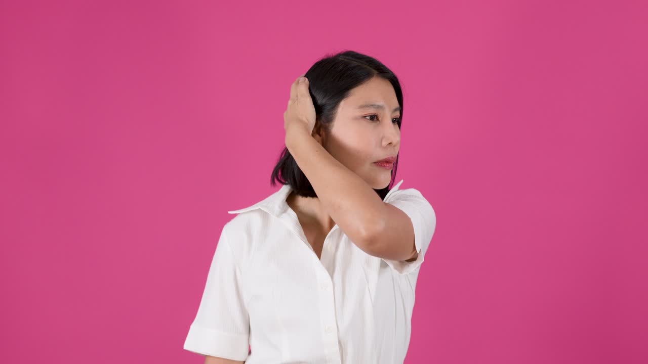 Mezza figura di una donna asiatica che si tocca i capelli e il viso con espressione pensierosa