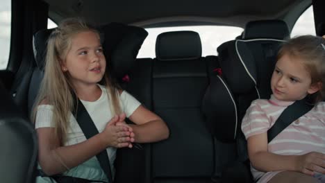 Two-caucasian-female-children-riding-in-the-car-in-the-back-seat-and-singing.