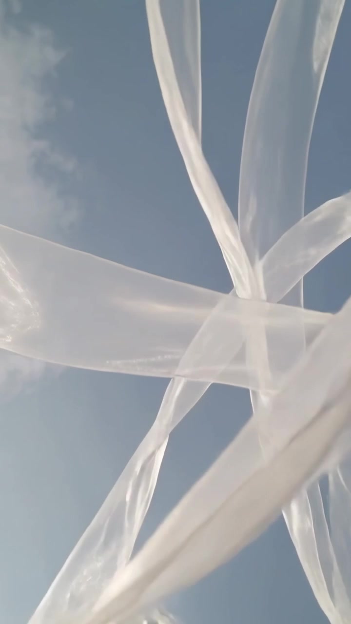 Vertical video: Fluttering sheer ribbons crossing blue sky, pushed by gusts, showing brown knots