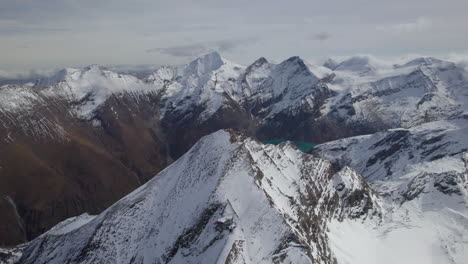 Majestic-snowy-mountains-of-Austria-and-Green-Lake-in-the-valley-during-sunny-day---Aerial-forward-flight