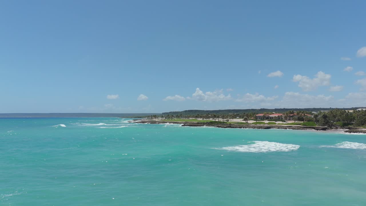 Scenic drone flight over ocean near beachfront resort showing golf course and natural shoreline