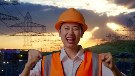 close up of asian female engineer with safety helmet screaming goal and dancing celebrating near high voltage tower