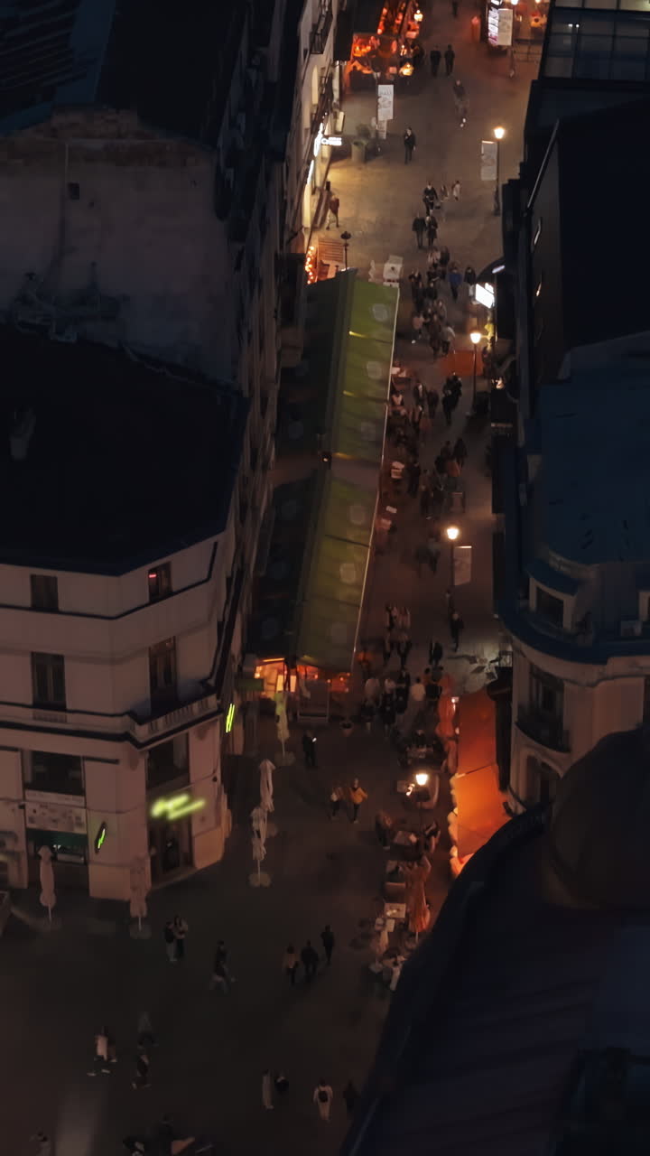 Vertical aerial drone view of walking people among old historical buildings and commercial shops in the old town in the evening. Blue hour in Bucharest, Romania