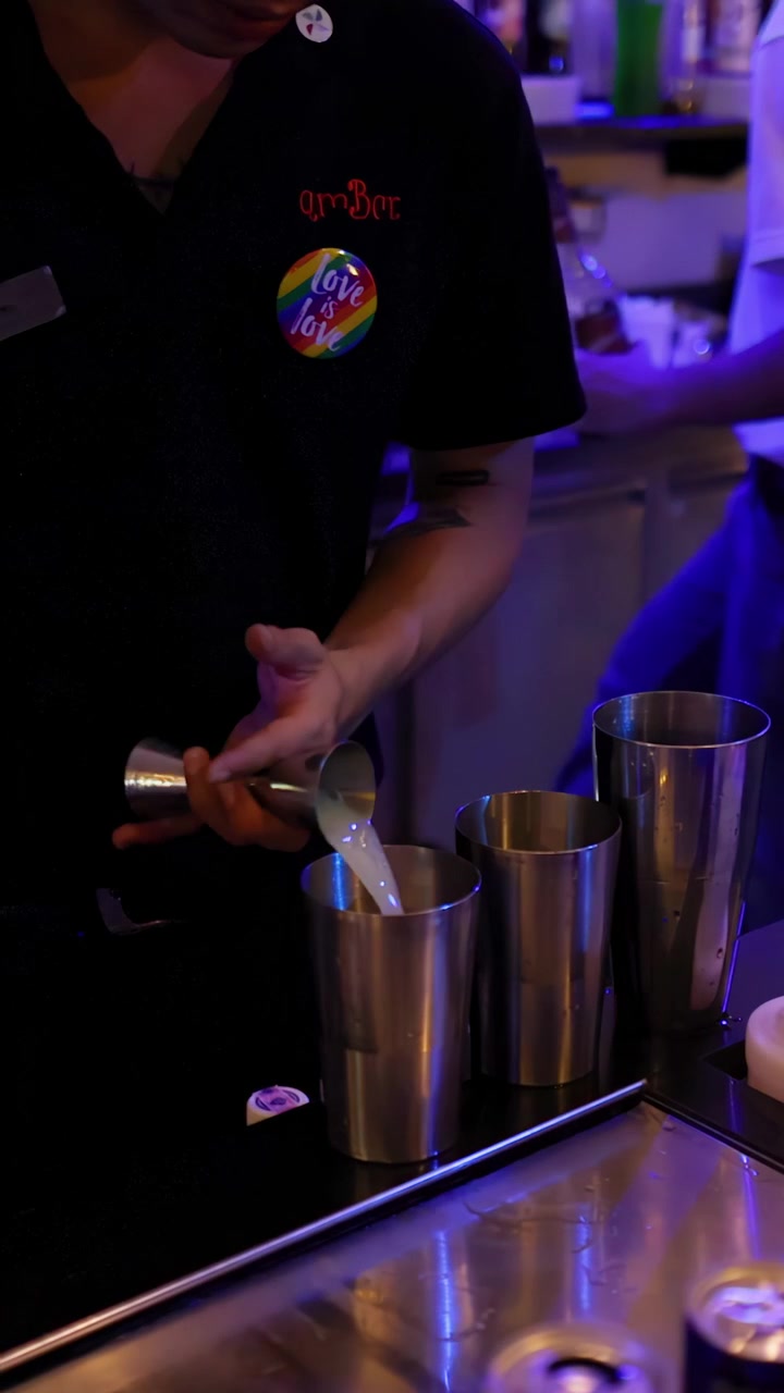 Un barman versa un liquore cremoso nello shaker sotto l'illuminazione colorata del bar, mentre prepara un cocktail a Bangkok.