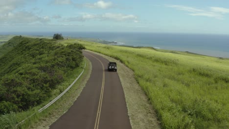 4k-aerial-of-car-driving-down-grassy,-country-road-in-Summer