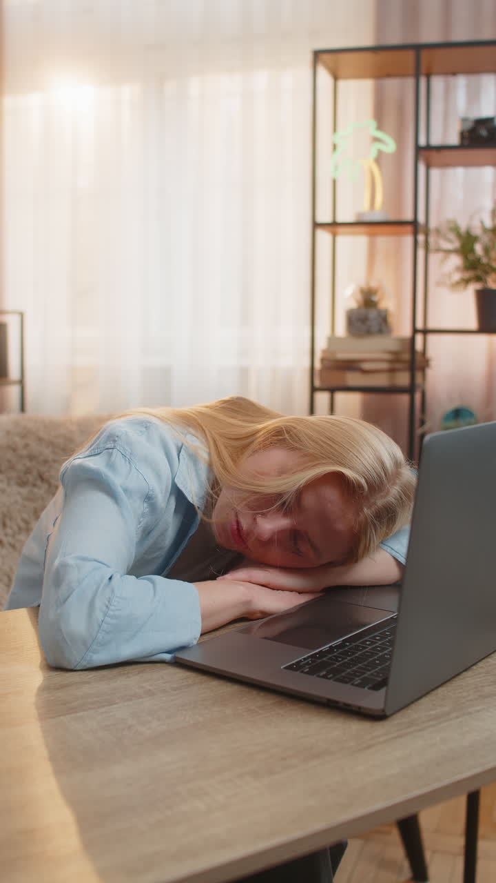 Tired young woman working on laptop exhausted at home wireless headphones fatigue falling asleep