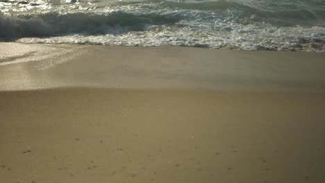 Close-up-of-the-sand-in-the-Portuguese-shore,-with-the-ocean-water-and-foam