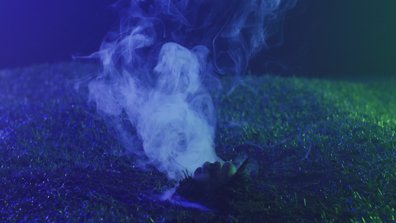 Video of hand raising from grass with smoke on black background
