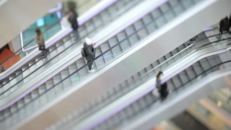 personas en movimiento en escaleras mecánicas en el centro comercial moderno. disparo con lente de cambio de inclinación con profundidad de campo súper superficial.