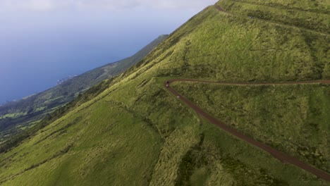 quad bikes on dirt road sided by lush green and dramatic cliff views of the atlantic ocean in são jorge island, the azores, portugal