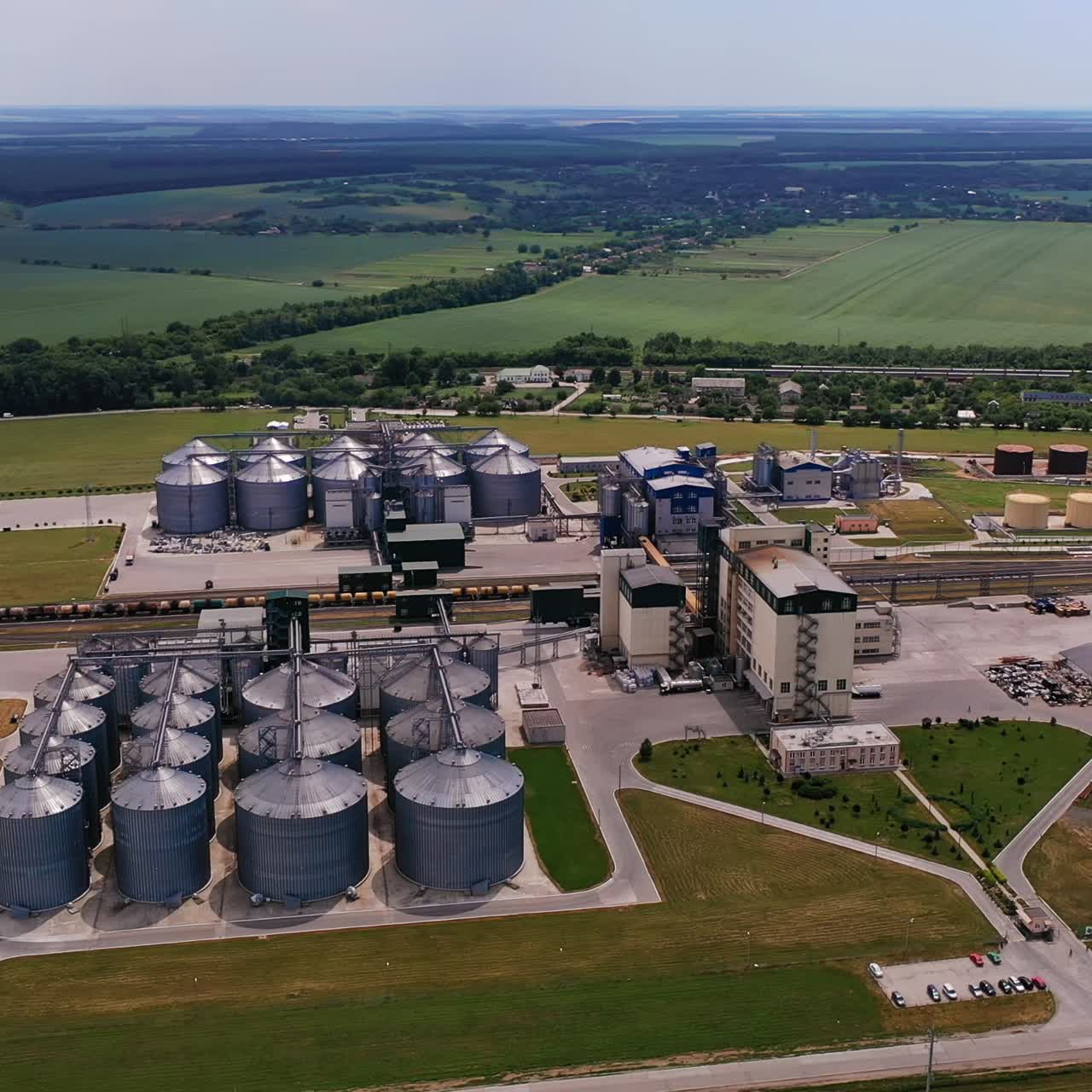 Enormous agricultural granary complex in the farmlands. Aerial view. Green fields and forests at the background
